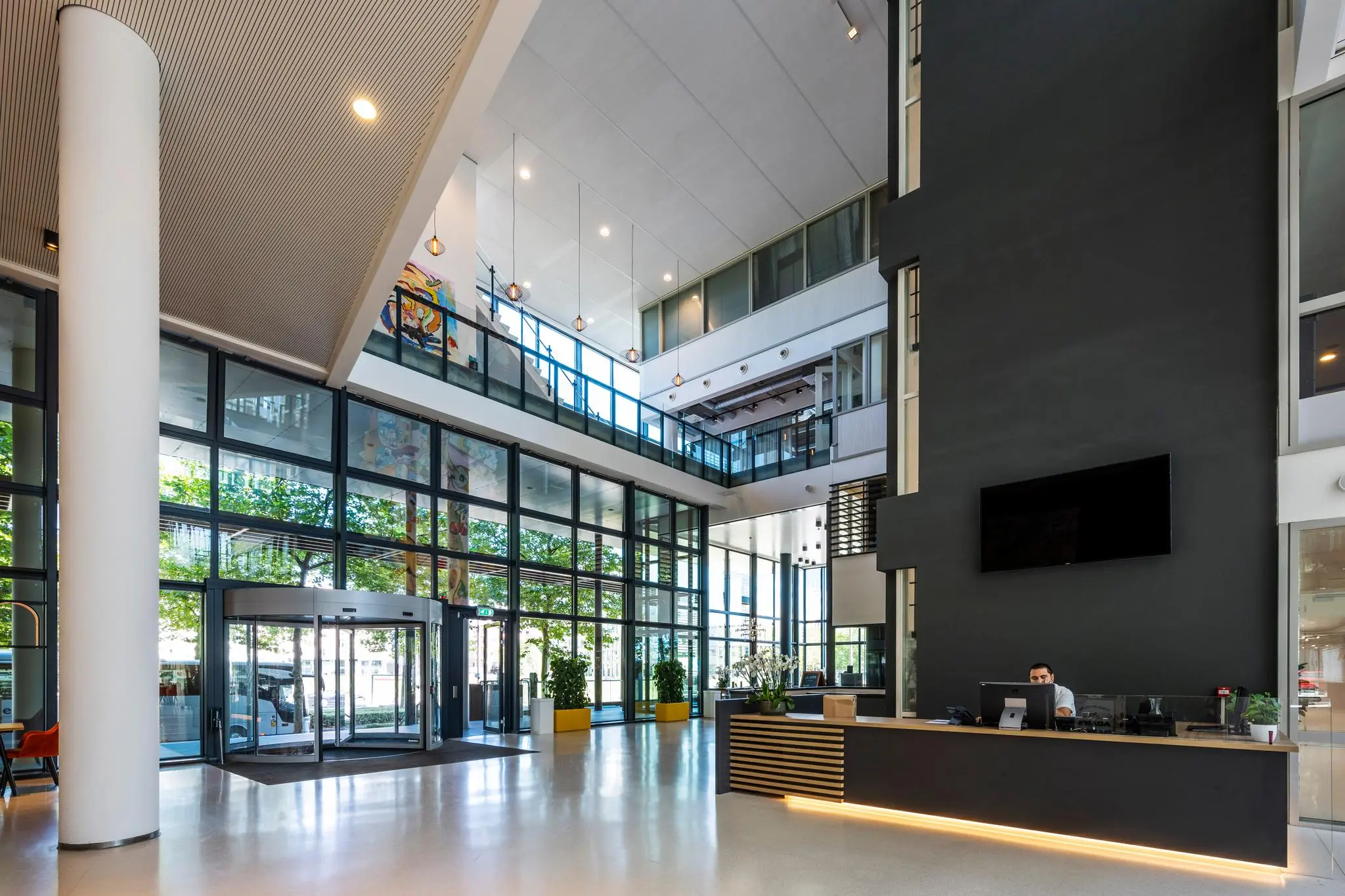 Moderne en ruime entreehal van een kantoorgebouw aan de Thomas R. Malthusstraat met glazen gevel, ontvangstbalie en vide.